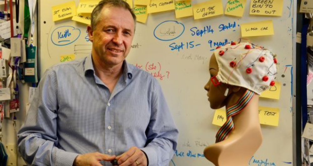 Prof Alan Smeaton standing in fron of a whiteboard beside a brainwave sensor