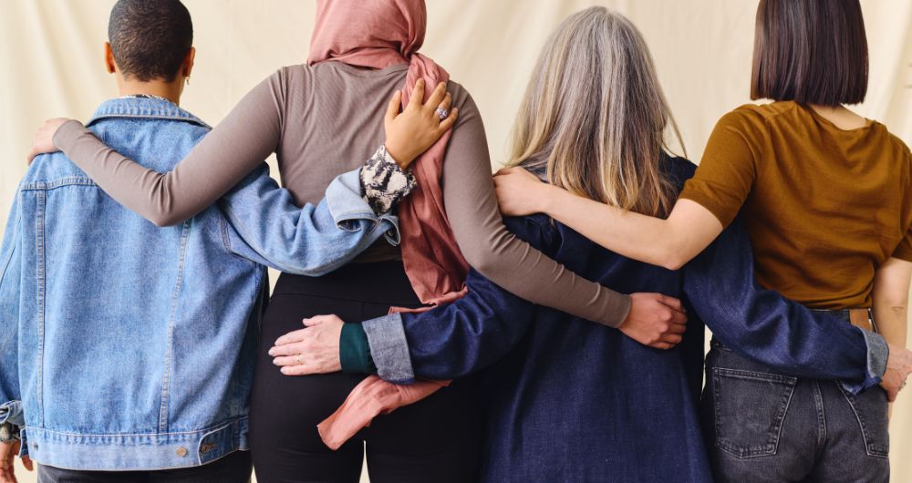 Group of four women, arm in arm, photographed from behind