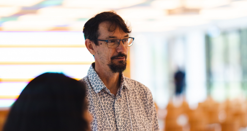 Ian Wood, Inisght Amlum, standing in front of a blurred side profile of a woman